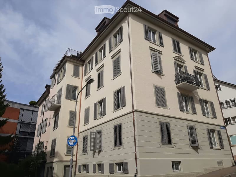 Four-story residential building with light beige facade, multiple windows with shutters, and balconies on upper floors.