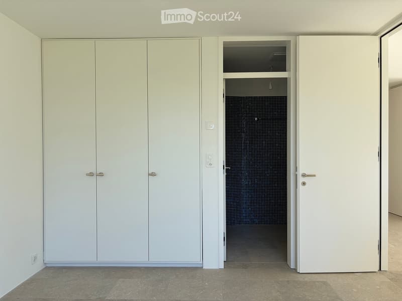 Empty room with white built-in wardrobes and a doorway leading to a tiled bathroom area.