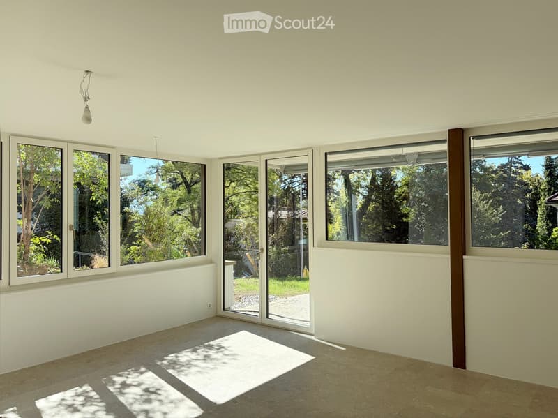 Empty room with large windows and sliding glass doors leading to an outdoor area, featuring light-colored walls and a tiled floor.