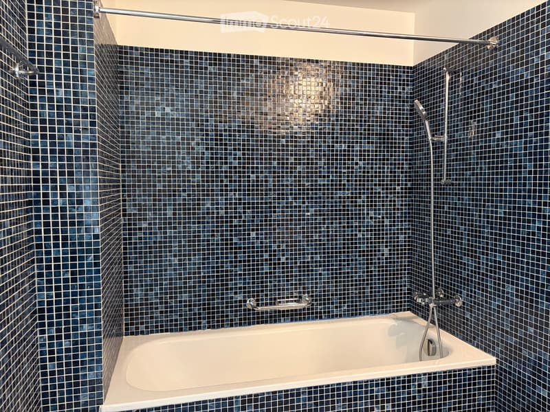 Bathtub with modern dark blue tiles, showerhead, and handrail.