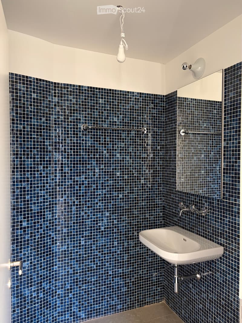 Modern bathroom with dark blue mosaic tiles, white sink, and sleek fixtures.