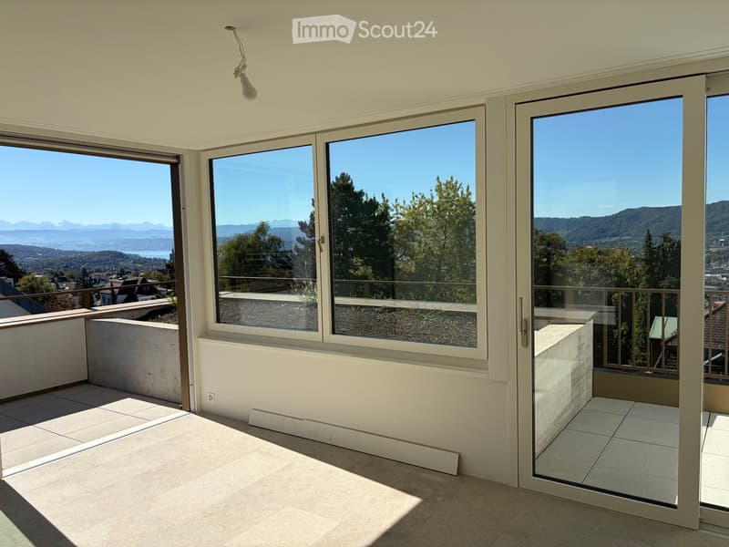 Bright, spacious balcony with large glass doors, tiled floor, and expansive scenic views of mountains and cityscape.