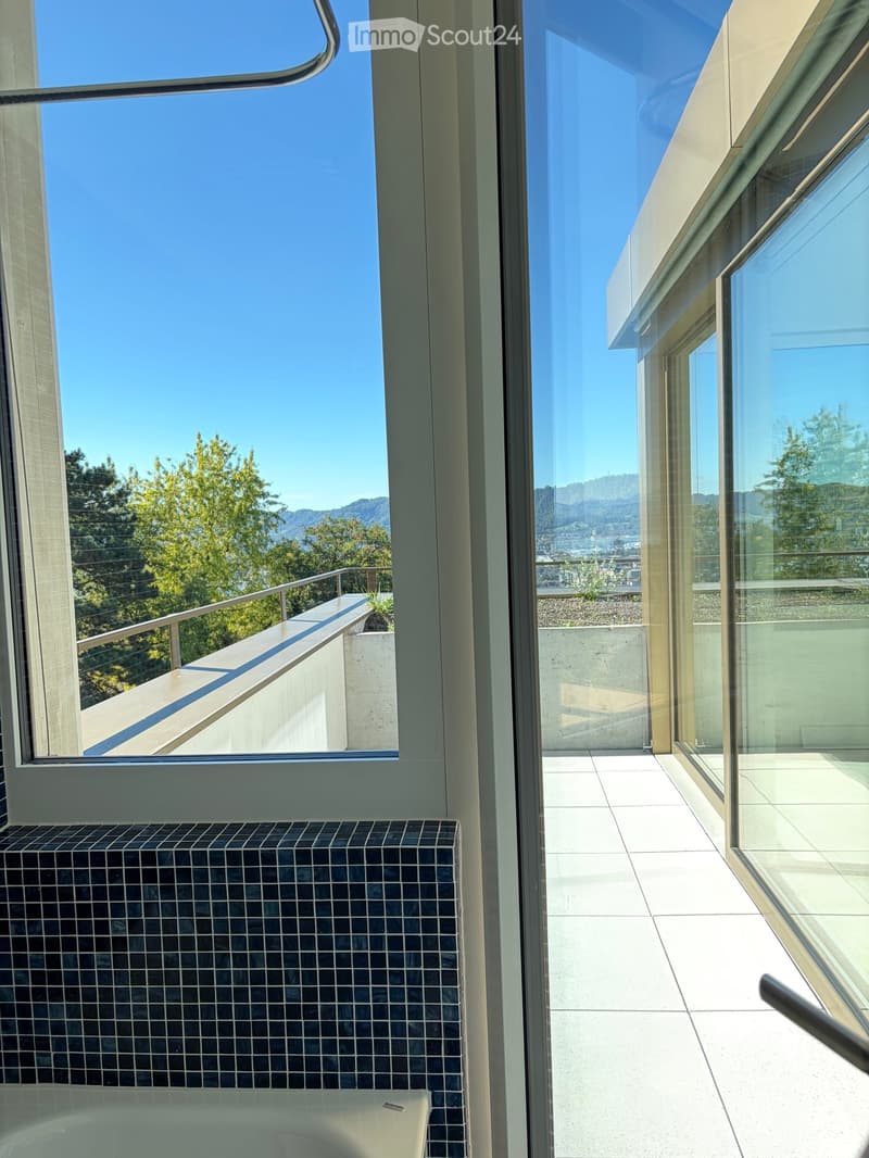 Modern bathroom with a bathtub, large windows offering a scenic view of trees and mountains, and a tiled floor.