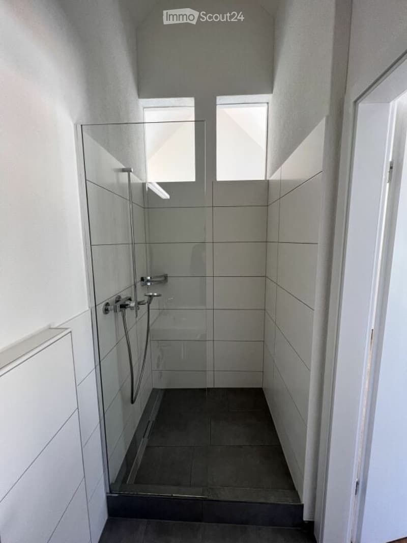 Modern bathroom with a glass-enclosed shower stall, dark tiled floor, and white tiled walls.