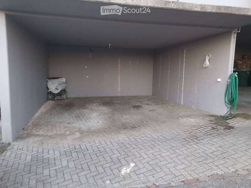 Empty outdoor space with brick pavement, grey walls, and a covered area. No furniture or equipment present.