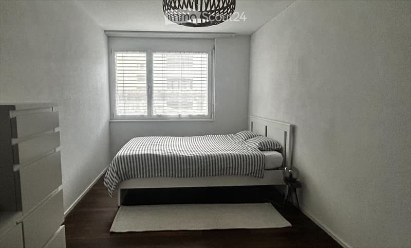 Minimalist bedroom with a single bed, white headboard, striped bedding, a small nightstand, and a woven pendant light fixture.