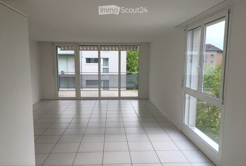 Empty room with tiled floor, large windows, and sliding glass doors leading to a balcony.