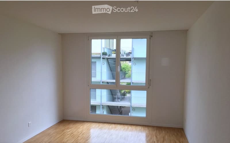 Empty room with wooden flooring and large windows showing a view of a staircase and outdoor area.
