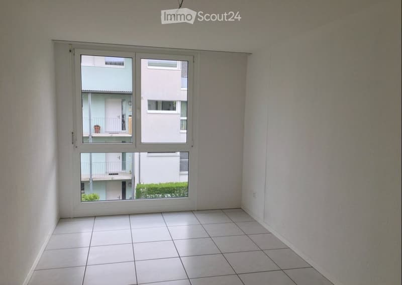 Empty room with white tiled floor and large window showing neighboring buildings and greenery.