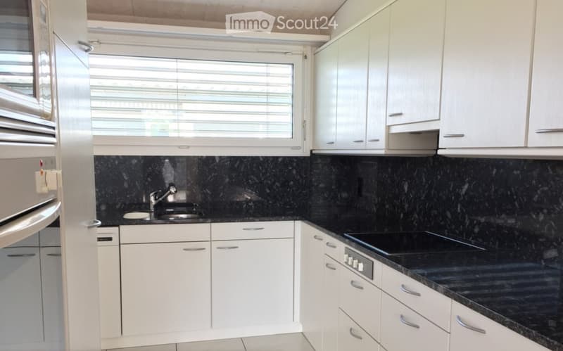 Modern kitchen with white cabinets, black granite countertops, stainless steel appliances, and a window with blinds.