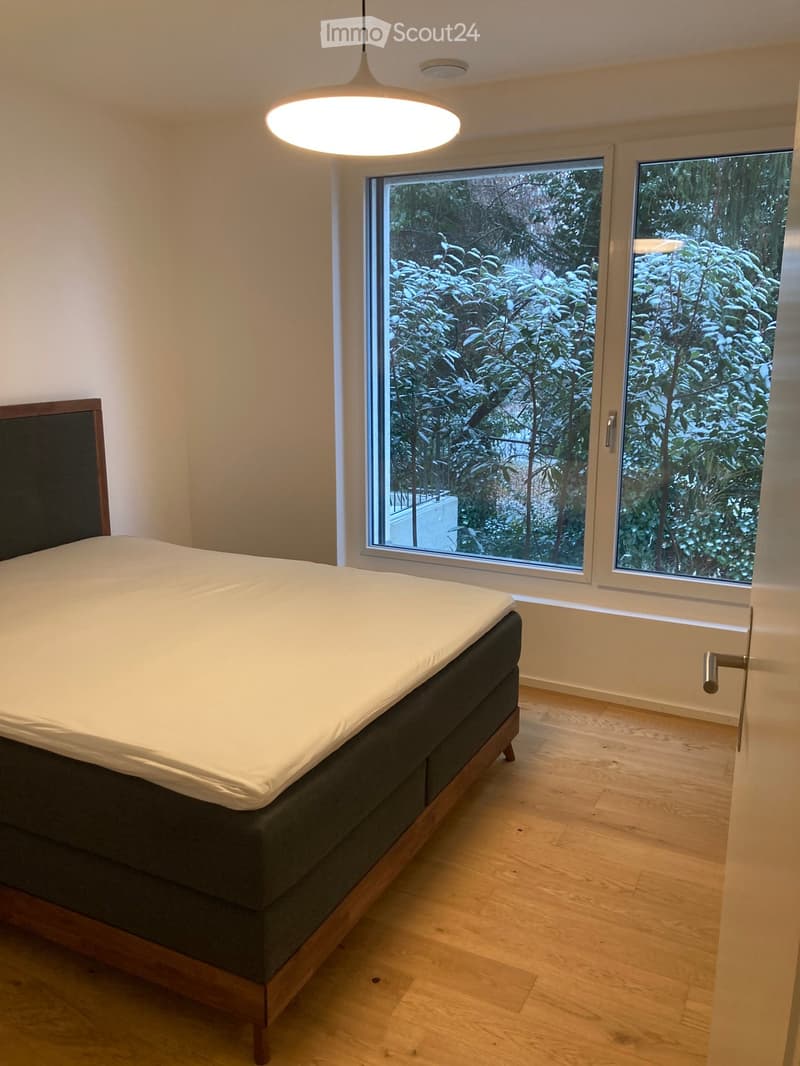 Minimalist bedroom with a single bed, wooden floor, large windows overlooking a snowy outdoor area, and a modern pendant light.