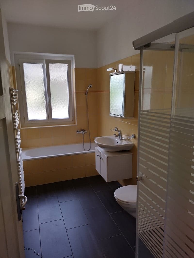 Bright bathroom with yellow tiles, black floor, bathtub, sink, toilet, and shower area.