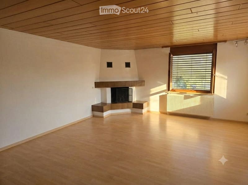 Empty room with wooden flooring, white walls, a fireplace, and a large window with blinds.