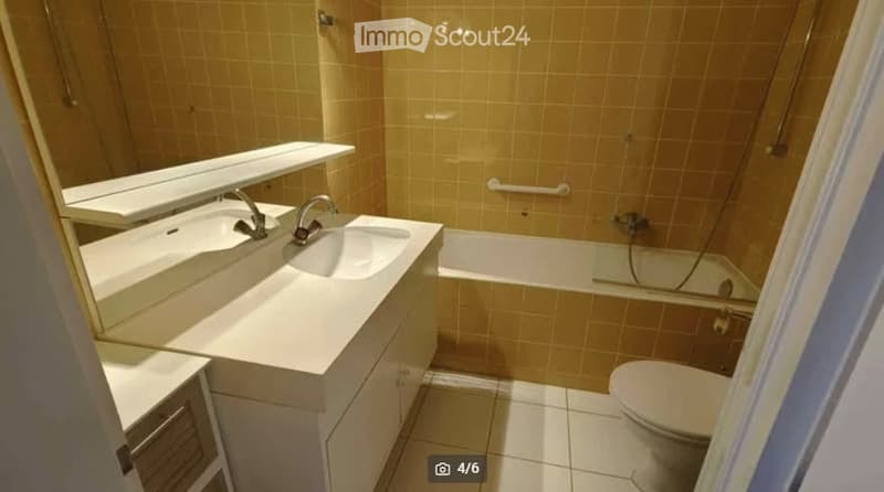 Modern bathroom with double sink, large mirror, bathtub, and toilet. Light-colored tiles and clean, contemporary design.