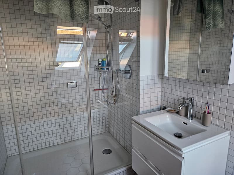 Modern bathroom with a white tiled shower stall, a white sink with a chrome faucet, a large mirror, and a towel hanging on the wall.