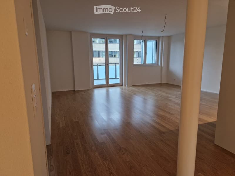 Empty room with wooden flooring, white walls, and large windows with a sliding glass door leading to a balcony.