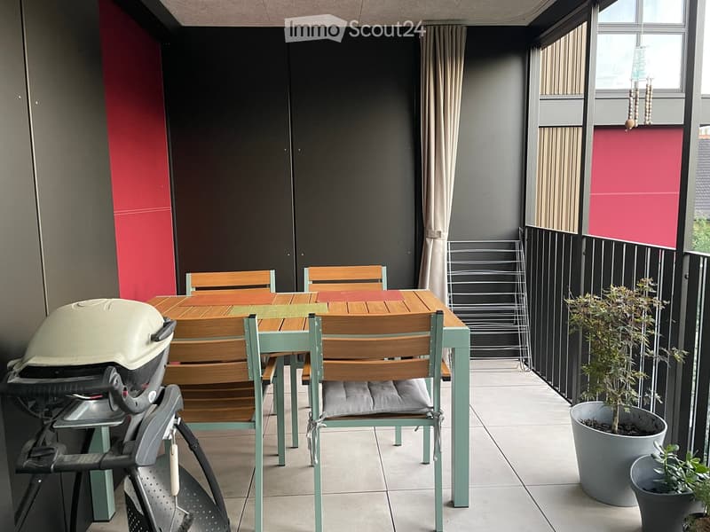 Balcony with a wooden table, chairs, a grill, and potted plants.