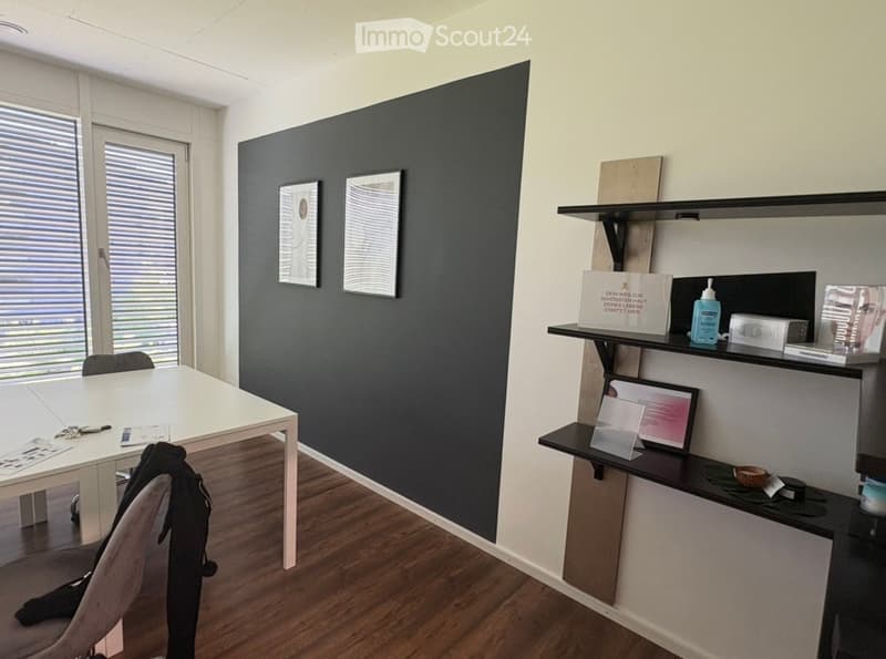 Modern office or meeting room with a white table, black chair, floating shelves, framed artwork, and a sign on the shelf.