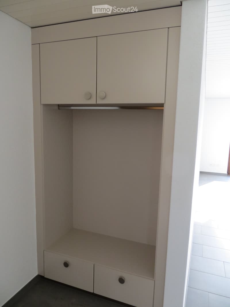 Empty built-in closet with two doors and two drawers, light-colored wood finish, white walls, and tiled floor.