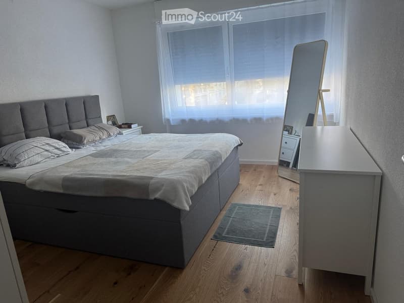 A modern bedroom with a large bed, a nightstand, a mirror, a small table, and a rug on a wooden floor.