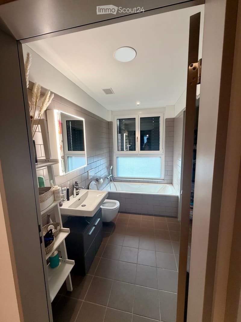 Modern bathroom with a sink, toilet, bathtub, and large window. Includes a mirrored cabinet, shelves with baskets, and various toiletries.