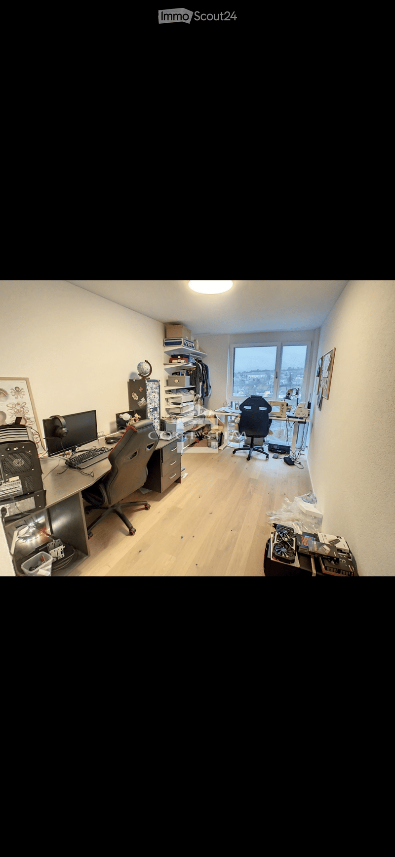 A well-lit, organized home office with wooden flooring, a large desk, two chairs, a computer setup, shelves, and a globe on display.