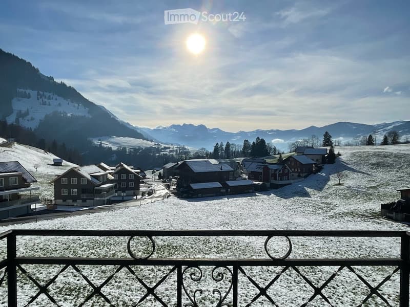 A scenic view of a snow-covered village with traditional houses, surrounded by snow-capped mountains under a clear blue sky.