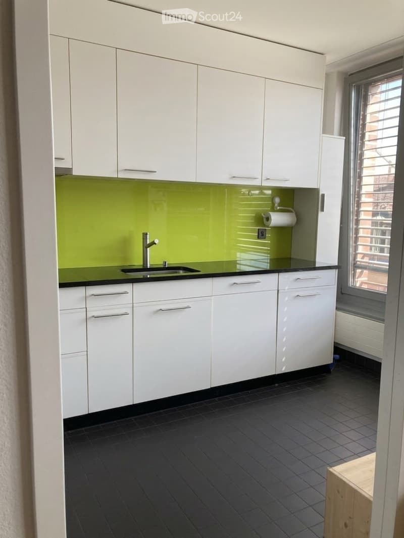 Modern kitchen with white cabinets, green backsplash, black countertop, and dark tiled floor.