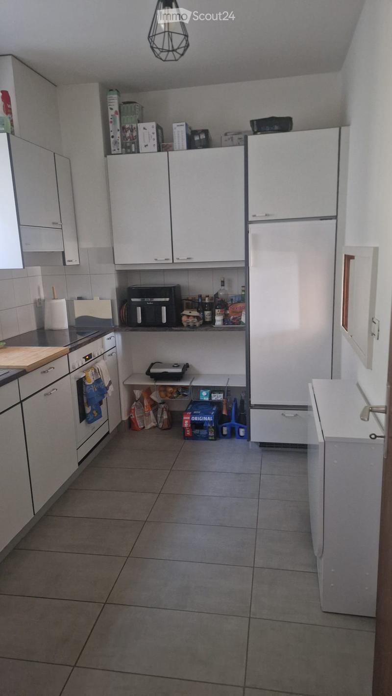 Modern kitchen with white cabinets, stainless steel appliances, tiled floor, and various items on the counter and shelves.