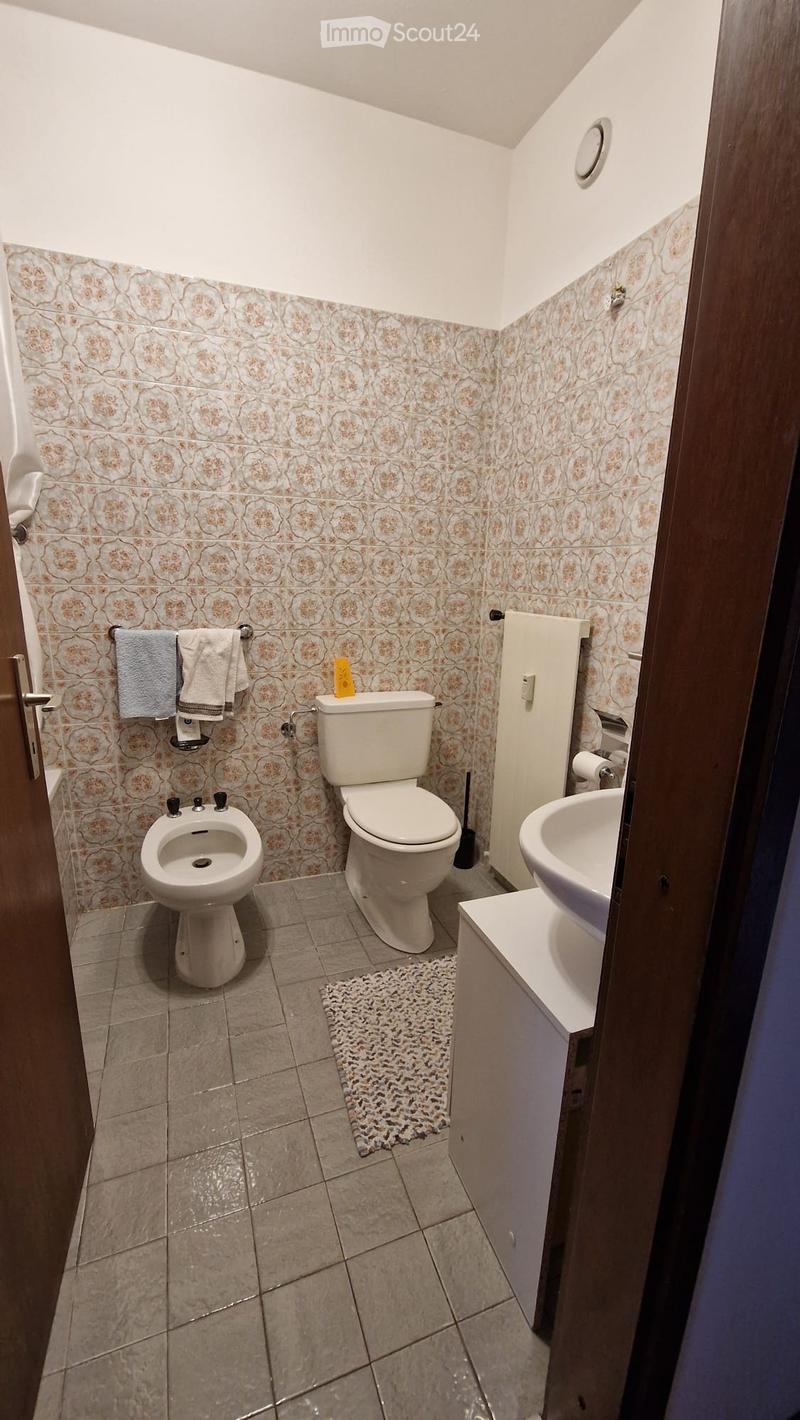 Bathroom with beige tiled walls, a toilet, bidet, sink, and a towel rack with towels.