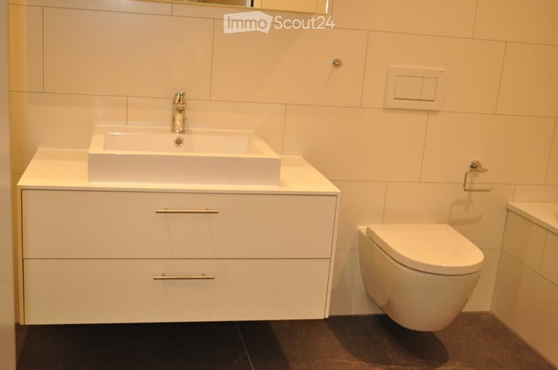 Modern bathroom with white tiles, a white sink with a chrome faucet, a white toilet, and a white cabinet with chrome handles.