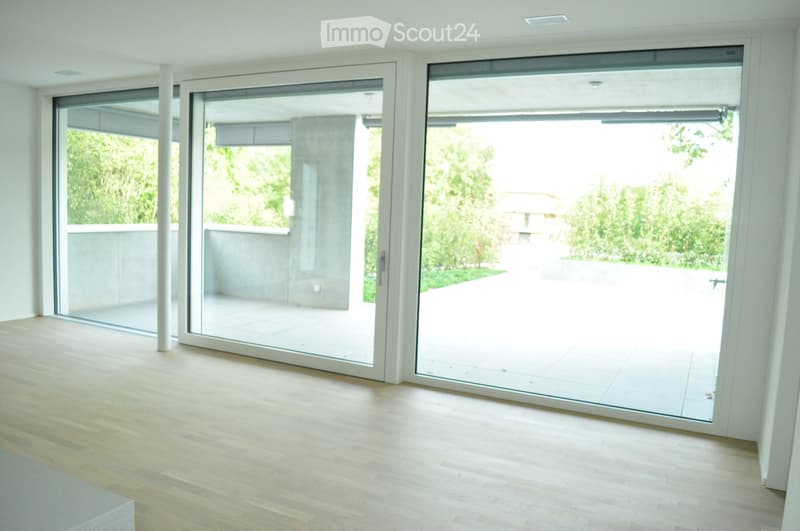 Empty room with light wooden flooring and large sliding glass doors leading to an outdoor patio area.