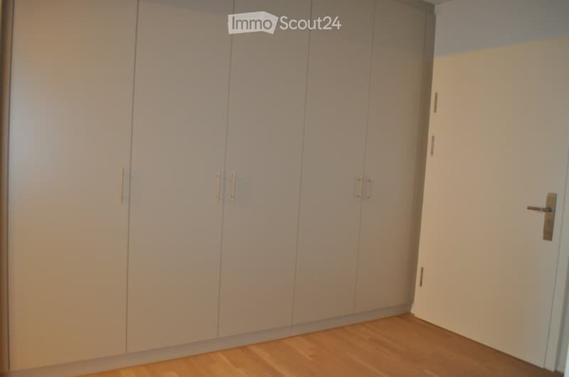 Empty room with light-colored wooden flooring and built-in white wardrobes with gold handles.