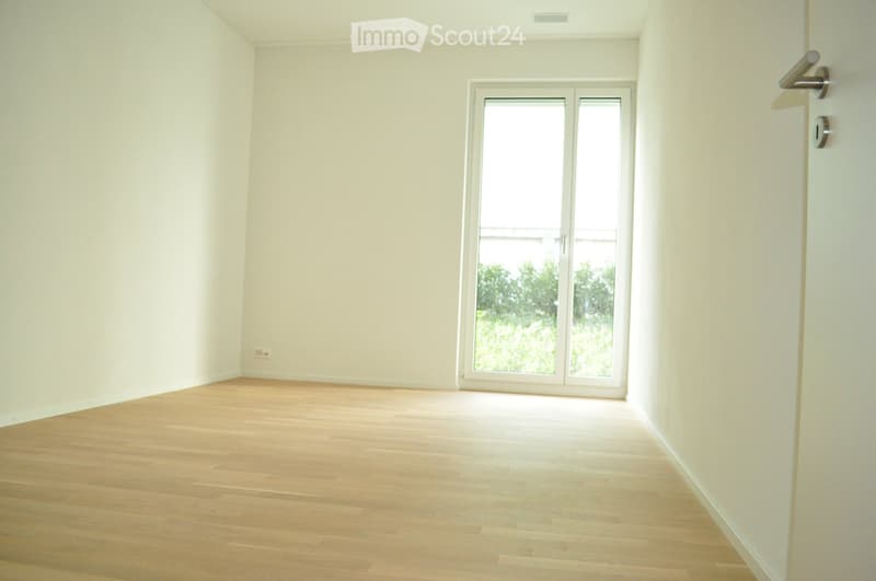 Empty room with light-colored wooden flooring and white walls, featuring a large sliding glass door leading to an outdoor area.