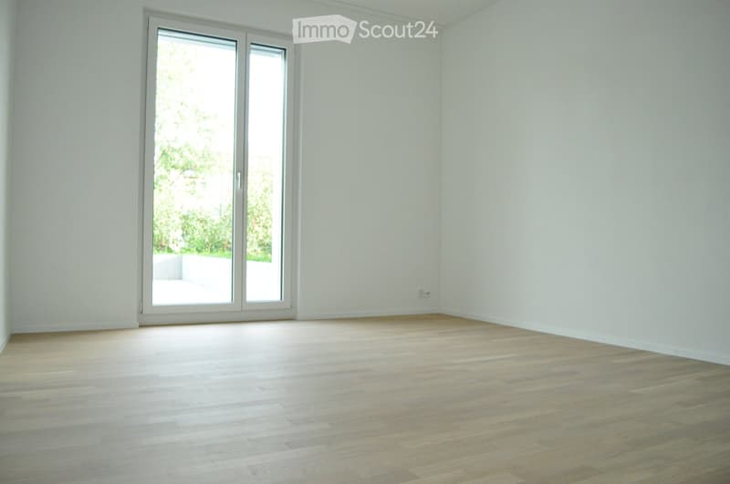 Empty room with light wooden flooring and white walls, featuring a large sliding glass door that opens to a balcony or outdoor area.