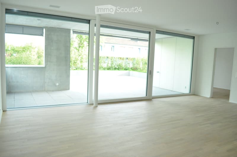 Empty room with light wooden flooring, large sliding glass doors leading to a balcony, and white walls.