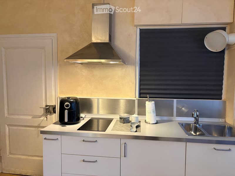 Modern kitchen with white cabinets, stainless steel sink, air fryer, and a window with blinds.
