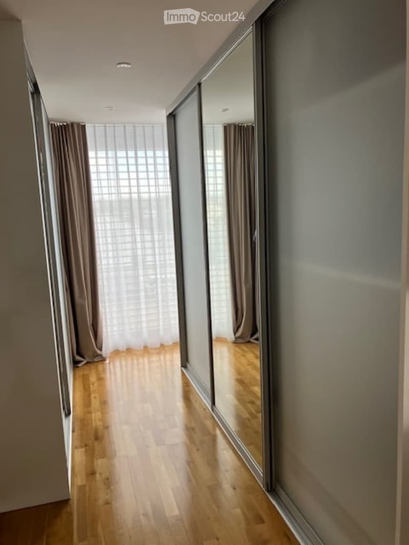 A modern hallway with wooden flooring, large mirrored closet doors, and sheer curtains allowing natural light to filter in.