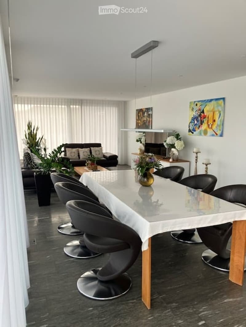 Modern dining and living area with a sleek white dining table, black chairs, a black sofa, and decorative artwork on the walls.