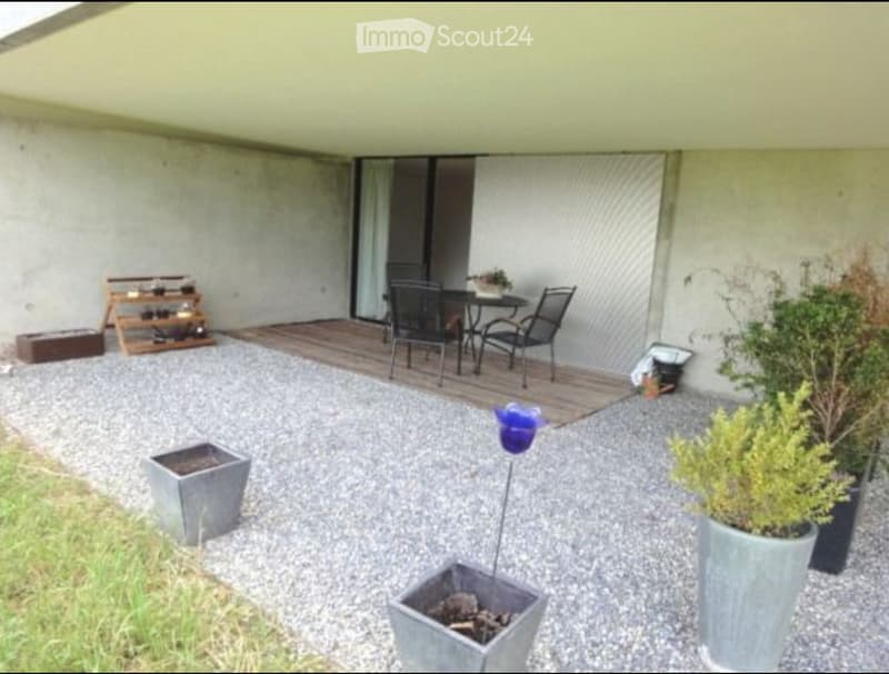 Outdoor patio area with gravel ground, wooden deck, small table and chairs, potted plants, and decorative items.