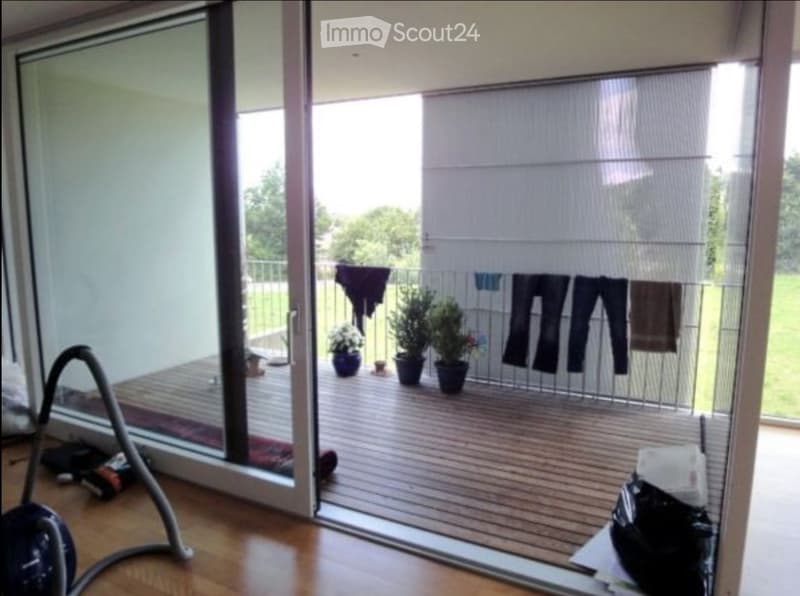 Balcony with wooden decking, potted plants, and a clothing rack with hanging items.