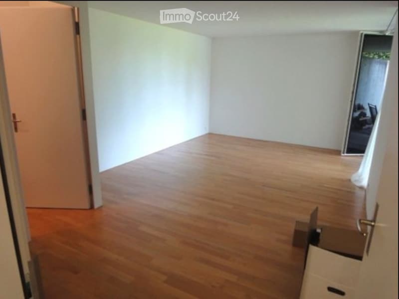 Empty room with wooden flooring and white walls, featuring a partially open door and a mirror on the wall.