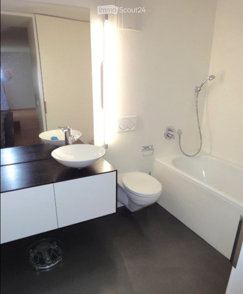 Modern bathroom with white walls, black floor, double sink vanity, toilet, bathtub, and showerhead.