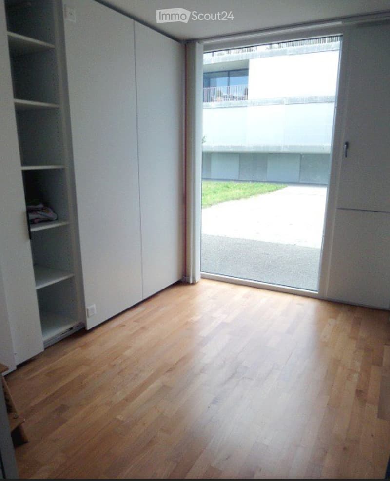 Empty room with wooden flooring, white walls, and a large sliding glass door leading to an outdoor area.