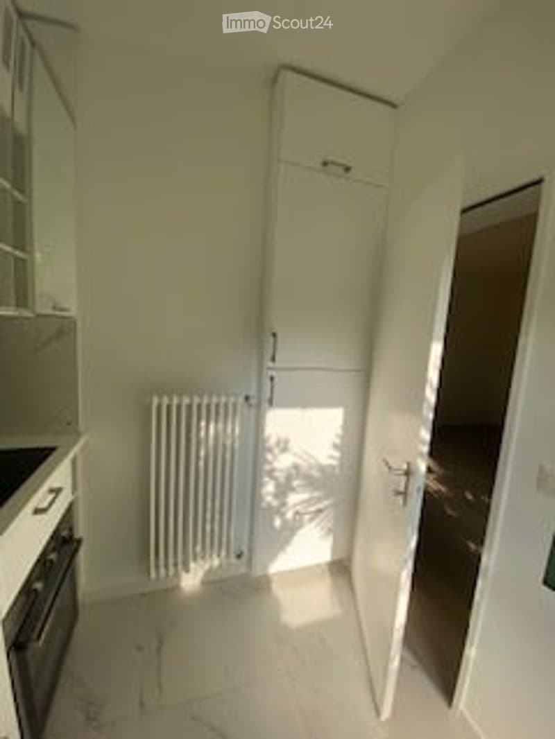 Empty room with white walls, tiled floor, radiator, and open door leading to another space.
