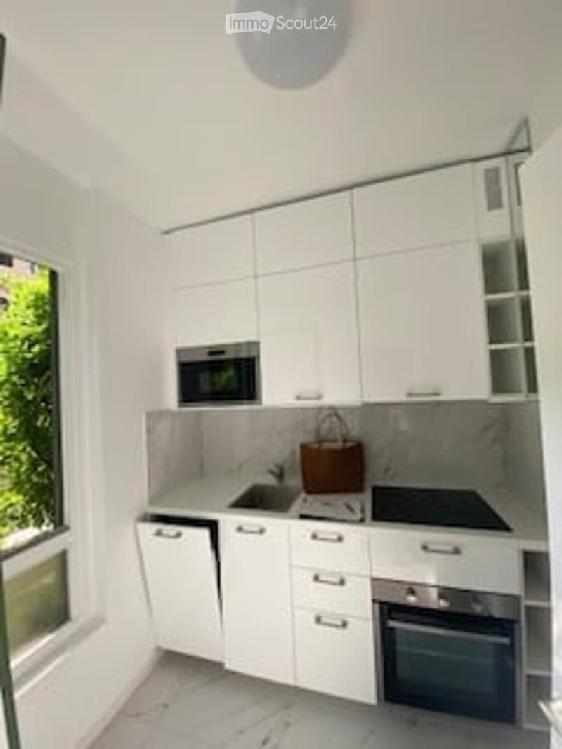 Modern, minimalist kitchen with white cabinets, stainless steel appliances, and a marble countertop.