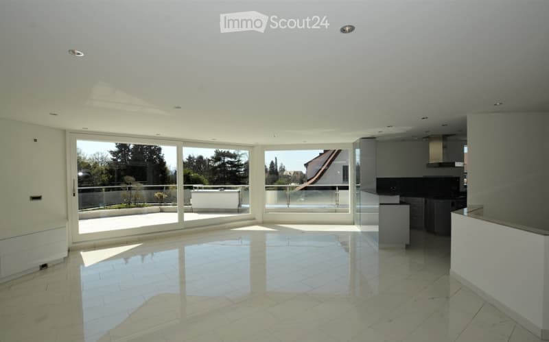 Bright, open-plan living and dining area with large glass sliding doors leading to a balcony, modern kitchen area with cabinets and island, polished tile flooring, recessed lighting.