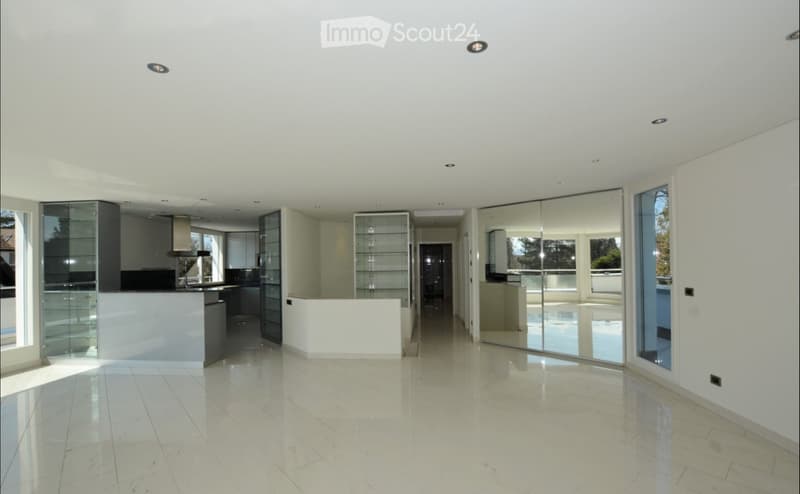 Open-plan, modern space with white walls, polished marble floors, large glass partitions, and recessed lighting. The area includes a kitchen area with cabinets and a countertop, but no furniture or appliances are present.