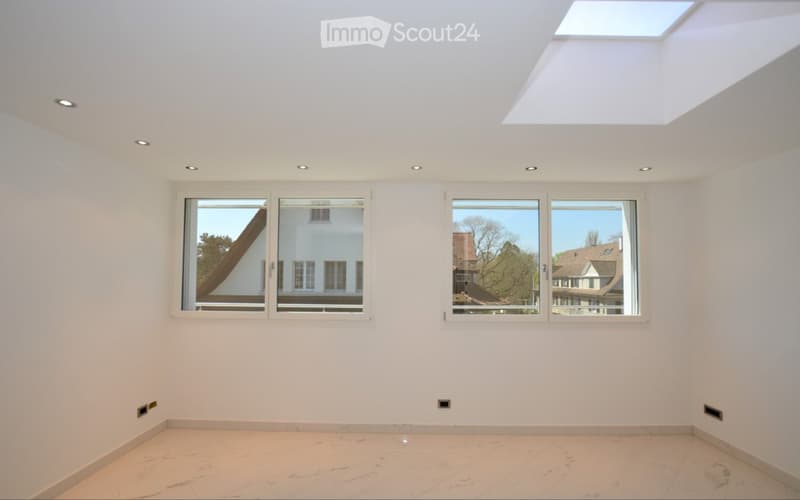 Empty room with white walls, light-colored tiled floor, large windows, and a skylight. No furniture or equipment present.