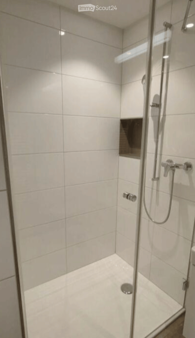 Modern shower stall with white tiles, glass enclosure, and a handheld showerhead.